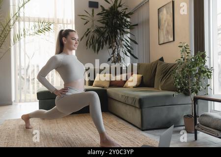 Healthy sport lifestyle concept, happy smiling girl doing sport and yoga exercises at green loft interior home watching and repeating trainer exercise Stock Photo