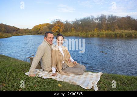 Young couple in love chilling by autumn lake. Happy man and woman enjoying nature and hugging. Romantic date Stock Photo