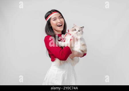 Lovely young Indonesian woman is holding a white ragdoll cat and smiling, isolated white background. Indonesia Independence Day and pets concept. Stock Photo