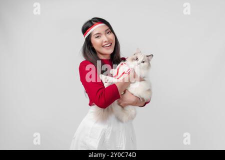Lovely young Indonesian woman is holding a white ragdoll cat and smiling, isolated white background. Indonesia Independence Day and pets concept. Stock Photo