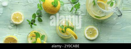 Lemonade with mint panoramic banner. Lemon water drink with ice. Two glasses and a pitcher on a blue background, overhead flat lay shot. Detox beverag Stock Photo