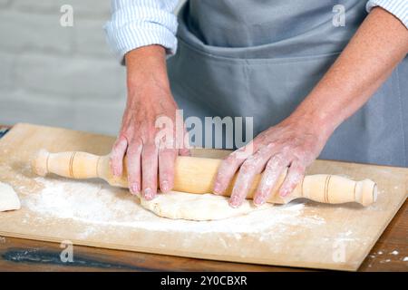 Chef rolling dough for pizza on a wooden table, female hands with rolling pin Stock Photo