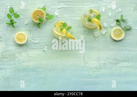Lemonade with mint. Lemon water drink with ice. Two glasses and lemons on a blue background, shot from the top with a place for text. Detox beverage. Stock Photo