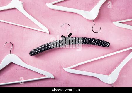 Exclusive fashion. Black satin hanger for delicate clothes surrounded by simple white hangers, a flat lay layout on pink. Shopping background, abstrac Stock Photo