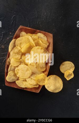 Potato chips in a wooden bowl, salty crisps, shot from the top on black with a place for text Stock Photo