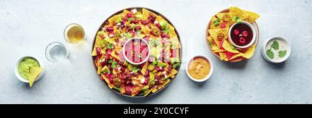 Loaded nachos panorama. Mexican nacho chips with beef, overhead flat lay shot with guacamole sauce, cheese salsa, tequila drinks, on a slate backgroun Stock Photo
