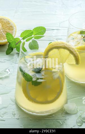 Lemonade with mint. Lemon water drink with ice. Two glasses and lemons on a blue background. Detox beverage. Fresh homemade cocktail Stock Photo