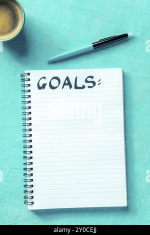Goals, handwritten word in a notepad with a ballpoint pen and a cup of coffee, shot from the top on a vibrant blue background. The concept of goal set Stock Photo