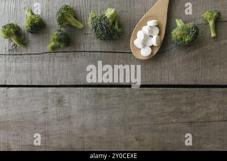 Vitamin or medicine capsules, broccoli on wooden spoon on wooden background. Health therapy or treatment concept. Vitamin pills. Stock Photo