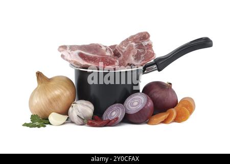 Black saucepan with pieces of raw pork inside. Around the saucepan are sliced vegetables which include onions, carrots, and garlic isolated on white b Stock Photo