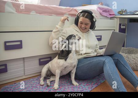 A teenager enjoys a moment of leisure in her room, working on her laptop and playing with her dog, creating an atmosphere of tranquility and happiness Stock Photo