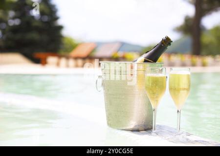 Champagne glasses and bottle in ice bucket near swimming pool. Vacation and romance concept Stock Photo