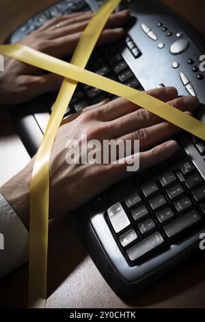 Close-up of a man's hand with duct tape typing at a computer keyboard Stock Photo