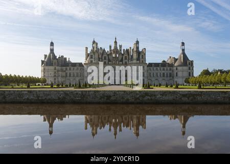 Impressive castle building with towers and windows, reflected in the calm water of the canal, under a blue sky, Chambord Castle, Chateau de Chambord, Stock Photo