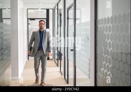 Portrait of serious male manager in glasses holding laptop and walking confidently in office corridor Stock Photo