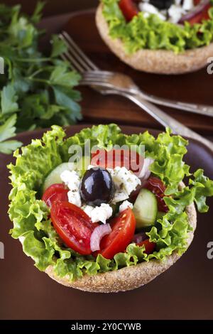 Close up of Greek salad in a bowl of whole-grain bread on wooden table, selective focus Stock Photo