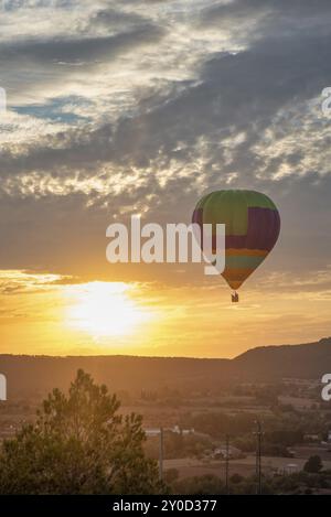 A colourful hot air balloon floats peacefully in a sunset sky with clouds and a hilly landscape Stock Photo