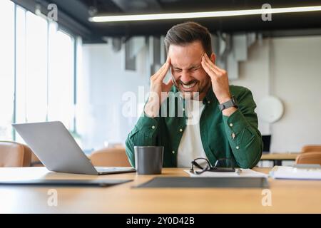 Frustrated furious young businessman with head in hands suffering from headache while working at desk Stock Photo