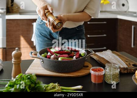 Close-up view of female hands sprinkle pepper from manual spice mill on vegetables in a baking pan Stock Photo