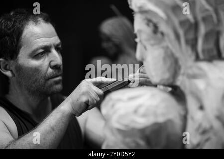 Close up of an artist's hands as they work on a wooden statue, using a chisel to shape the wood with precision. The black and white image captures the Stock Photo