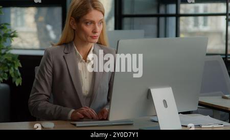 Caucasian middle-aged woman in office working with online project. Business female work in Internet communicate with clients distant with computer Stock Photo