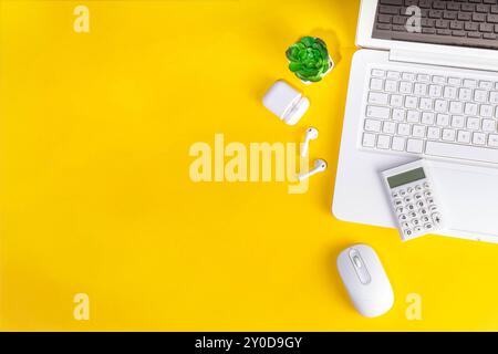 Stylish bright yellow minimalistic office workplace with notebook keyboard, office plant, earphones, calculator, flat lay style top view copy space Stock Photo