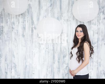 Portrait of beautiful smiling pregnant woman wearing casual jeans over wooden white background Stock Photo