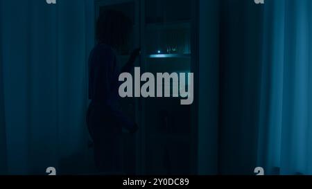 Confused unrecognizable woman girl walking in dark room night war blackout trouble search with light check closet electricity energy crisis outage Stock Photo