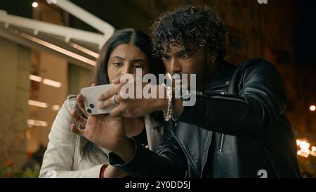 Confused puzzled man woman tourist travelers in night evening city Indian Arabian couple lost in street town travel tour trip guy girl using mobile Stock Photo