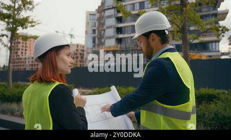 Two contractors civil engineers checking information in blueprint discuss teamwork pointing city buildings project managers planning collaboration Stock Photo