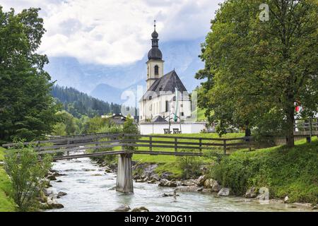 Parish church of St Sebastian by a river in an idyllic Alpine landscape with mountains and forests in the background, bridge, Ramsau, Berchtesgadener Stock Photo