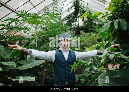Handsome businessman standing in botanical garden, in the middle of lush green foliage, using VR headset. Stock Photo