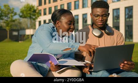 Two African American friends students high school pupils classmates university college academy in park outdoors learning studying together laptop Stock Photo