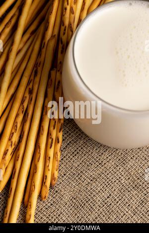 Thin and long bread sticks made of wheat flour and a glass of milk , sweet wheat pastries on the table with cow 's milk Stock Photo