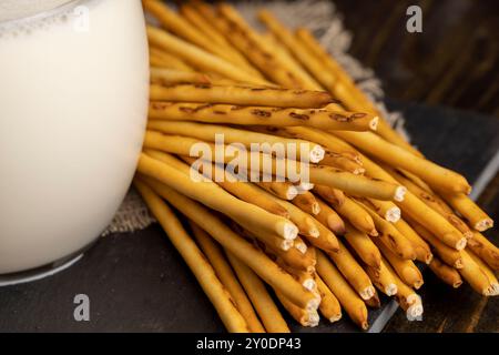 Thin and long bread sticks made of wheat flour and a glass of milk , sweet wheat pastries on the table with cow 's milk Stock Photo