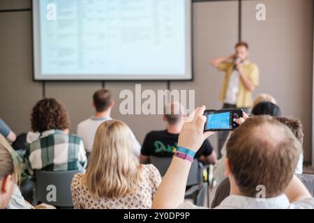 Engaged audience during a business presentation, with attendees capturing insights on mobile devices in a conference setting. Stock Photo