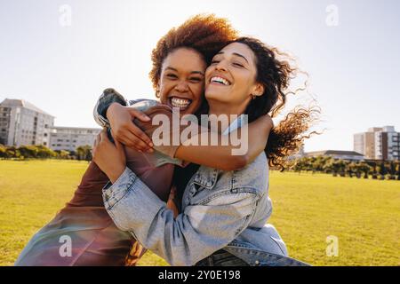 Two cheerful female students hugging in public park on a sunny afternoon, reflecting joy, friendship, and happiness. Stock Photo