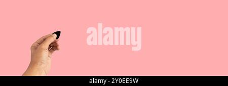 Black male hand holding a guitar pick isolated on pink background banner Stock Photo