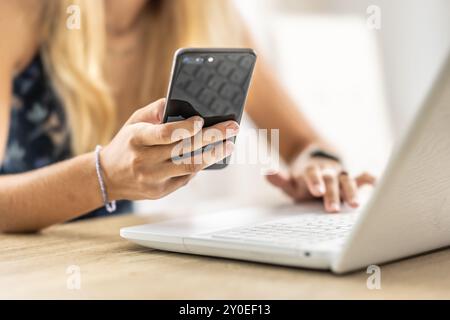 Female manager holds a smartphone in her hand and takes notes on the Laptop. Stock Photo