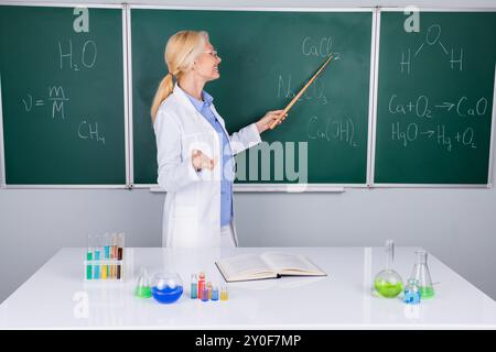 Photo of charming senior woman college professor in white coat explaining subject isolated on green board background Stock Photo