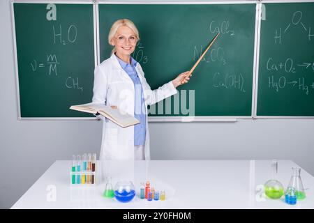 Photo of intelligent senior woman university lecturer in white coat explaining biology isolated on green board background Stock Photo