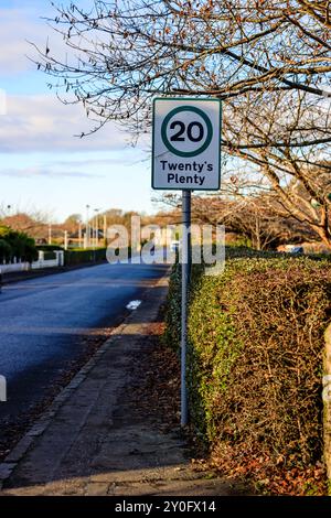 Twenty's Plenty speed sign on a residential street devoid of traffic or people, on a sunny winter's day there are fallen leaves on the pavement. Stock Photo