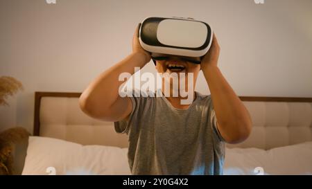 Funny enthusiastic smiling child kid boy schoolboy play video game using innovative digital VR goggles playing online 3d AR technology in metaverse Stock Photo