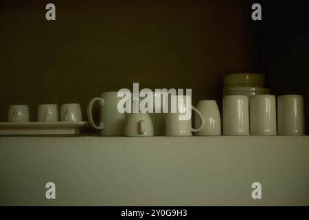 Modern white ceramic drinking glass and mugs set for kitchenware on wall shelves Stock Photo