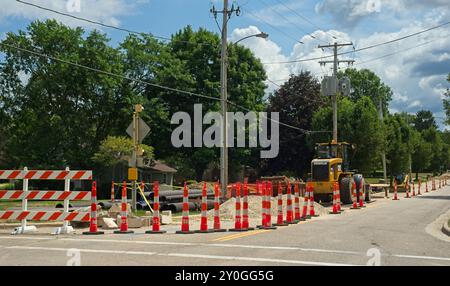 Road construction vehicles and other materials sit behind a barrier of traffic cones on a city street. Stock Photo