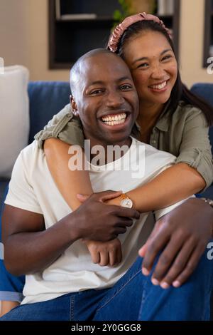 Smiling multiracial couple embracing on couch, enjoying quality time at home together Stock Photo