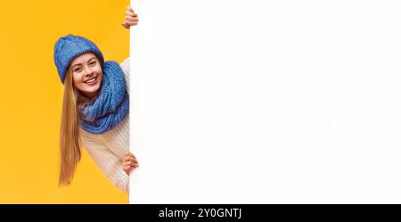 Blonde girl in winter hat staying next to blank board Stock Photo