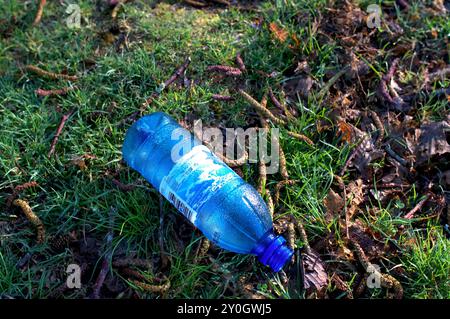 Discarded empty blue plastic water bottle on the ground with dew forming on the sides. Stock Photo