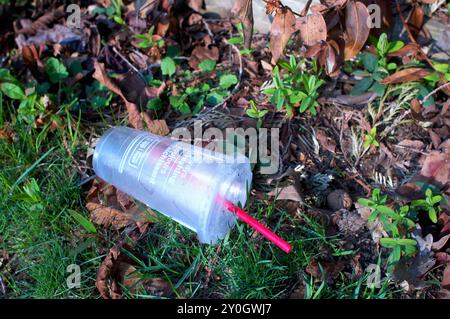 Discarded frosted plastic beverage container on the ground with lid and red plastic straw. Stock Photo