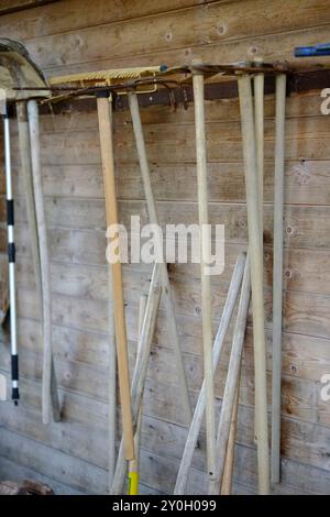 Various well used gardening tools are hanging on an old wooden wall, implying someone is taking good care of their equipment Stock Photo